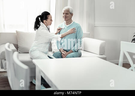 Grauhaariger bescheidener Mann sitzen und Krankenschwestern. Stockfoto