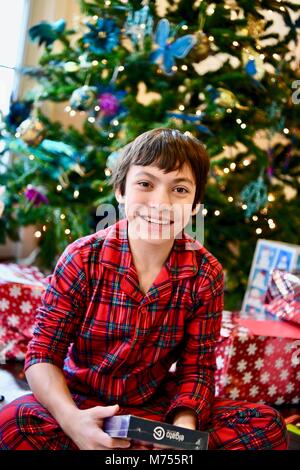 Jugendliche 10-14 auf Weihnachten Morgen neben dem Weihnachtsbaum mit Geschenken im Alter von Stockfoto