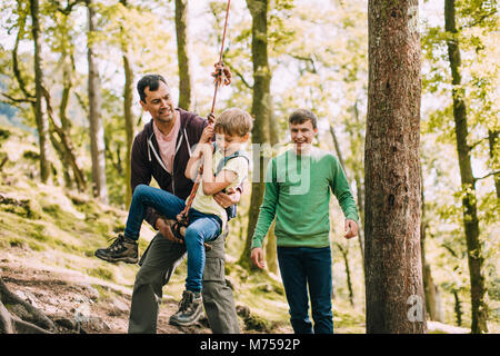 Kleiner Junge wird an einem Seil schwingen in den Wäldern von seinem Vater und Bruder geholfen. Stockfoto