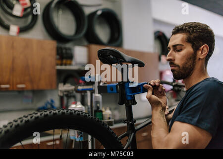 Arbeitnehmer Instandsetzung ein Fahrrad an der Werkstatt. Mann zur Festsetzung ein Fahrrad zu einem Betrieb stehen in einer Werkstatt. Stockfoto