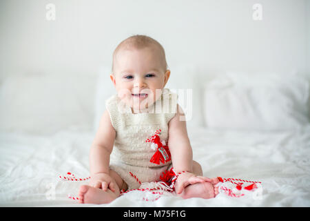 Cute Baby Kleinkind Junge, spielen mit weißen und roten Armbändern. Martenitsa, weiße und rote Sorten aus Garnen, bulgarischen Folklore Tradition, der Frühling Stockfoto