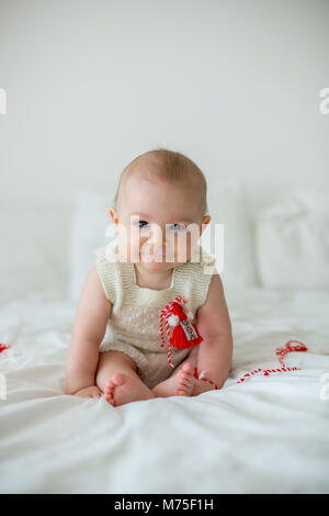 Cute Baby Kleinkind Junge, spielen mit weißen und roten Armbändern. Martenitsa, weiße und rote Sorten aus Garnen, bulgarischen Folklore Tradition, der Frühling Stockfoto