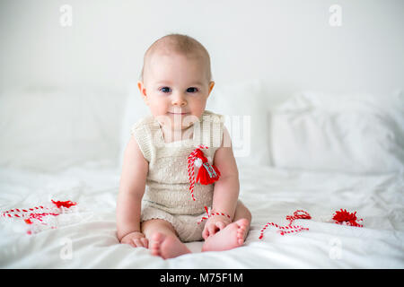 Cute Baby Kleinkind Junge, spielen mit weißen und roten Armbändern. Martenitsa, weiße und rote Sorten aus Garnen, bulgarischen Folklore Tradition, der Frühling Stockfoto