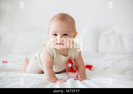 Cute Baby Kleinkind Junge, spielen mit weißen und roten Armbändern. Martenitsa, weiße und rote Sorten aus Garnen, bulgarischen Folklore Tradition, der Frühling Stockfoto