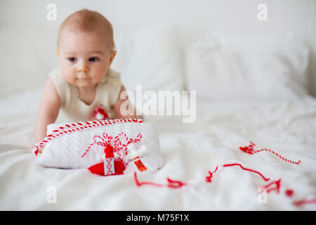 Cute Baby Kleinkind Junge, spielen mit weißen und roten Armbändern. Martenitsa, weiße und rote Sorten aus Garnen, bulgarischen Folklore Tradition, der Frühling Stockfoto