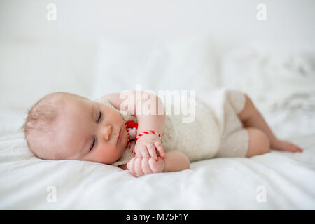 Cute Baby Toddler Boy, Schlafen mit weißen und roten Armband. Martenitsa, weiße und rote Sorten aus Garnen, bulgarischen Folklore Tradition, der Frühling Stockfoto