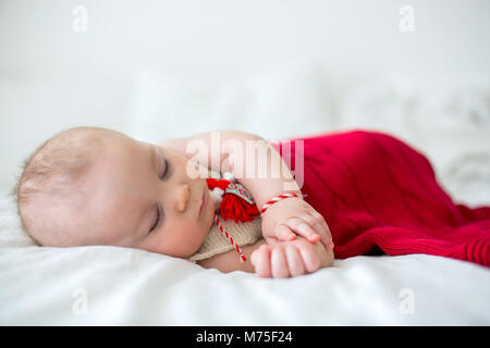 Cute Baby Toddler Boy, Schlafen mit weißen und roten Armband. Martenitsa, weiße und rote Sorten aus Garnen, bulgarischen Folklore Tradition, der Frühling Stockfoto