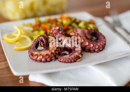 Makro Nahaufnahme von Octopus Vorspeise mit Gemüse, Zitrone und Kartoffeln auf einem Tisch mit einem Glas Wein Stockfoto