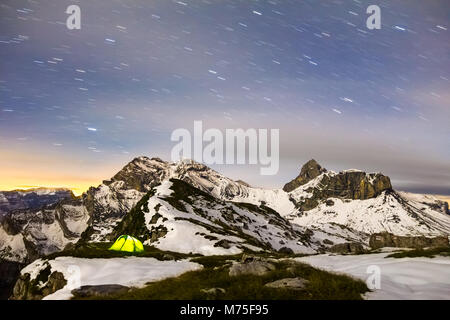 Zelt leuchtet unter einem Sternenhimmel in der verschneiten Bergwelt. Alpen, Schweiz. Stockfoto