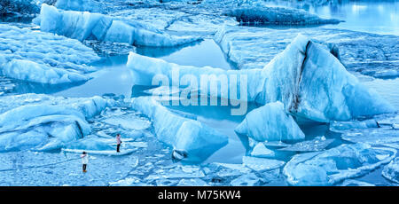 Gletscherlagune Jokulsarlon Panorama in der Dämmerung, in Island. Nicht identifizierbare Touristen zu Fuß auf dünnem Eis zu fotografieren, spektakuläre Eisberge. Stockfoto