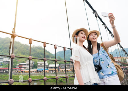 Junge asiatische schöne Backpackers unter selfie auf die hölzerne Hängebrücke jingtong, Taiwan. Im sonnigen Sommertag. Stockfoto