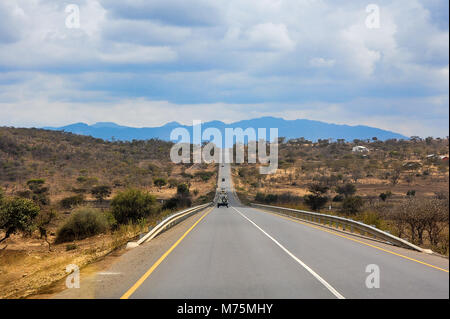Endlose Straße durch trockenen, staubigen Landschaft zwischen Kenia und Tansania, Ostafrika. Moody Wolken, die fernen Berge, ebenen Landschaft Stockfoto