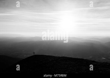 Kreuz auf dem Gipfel des Mt. Serrasanta (Umbrien, Italien), mit Sun niedrig am Horizont Stockfoto