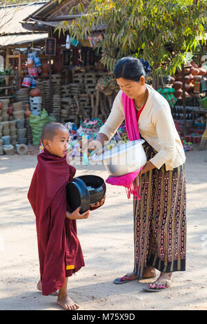 Novize buddhistischen Mönch sammeln Almosen in Bagan, Myanmar (Burma), Asien im Februar - lokale Frau geben Reis und Essen Stockfoto