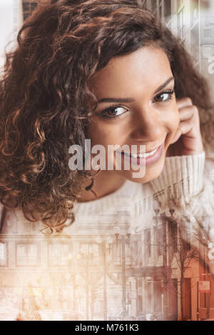 Angenehme fröhliche Frau, die gerne beim Sitzen und Lächeln Stockfoto