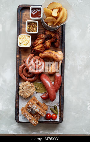 Fleisch für ein großes Unternehmen, das auf einem Holzständer. Gegrillte Würstchen, Sauerkraut, Pommes frites und Saucen. Ansicht von oben Stockfoto