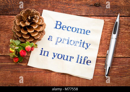 Wird eine Priorität in Ihrem Leben inspirational Handschrift auf eine Serviette auf einem rustikalen Holztisch Stockfoto