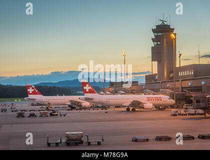 Flughafen Zürich bei Sonnenuntergang mit zwei Schweizer Airline Flugzeuge und der Tower. Stockfoto