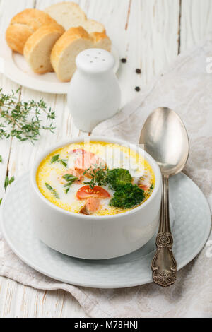 Chowder mit Forellen und Gemüse - Kartoffeln, Karotten, Tomaten und Brokkoli in einer weißen Schüssel auf hellem Holztisch Stockfoto