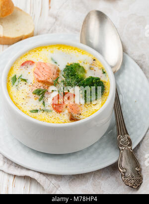 Lachs cremige Suppe mit Gemüse - Kartoffeln, Karotten, Tomaten und Brokkoli in einer weißen Schüssel auf hellem Holztisch Stockfoto