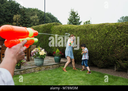 Sicht der Schuß von einem Mann mit einem Wasser Kampf mit Wasserpistolen im Garten, der mit seiner Frau und seinem Sohn. Stockfoto