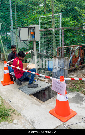Zwei Techniker arbeiten auf dem Bürgersteig durch ein Mannloch. Stockfoto