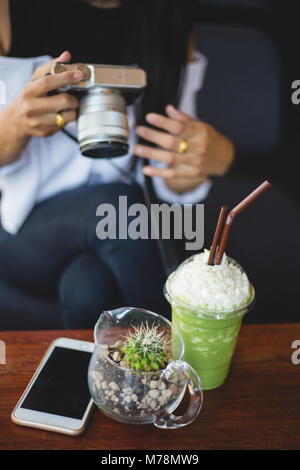 Frau ein Foto mit Matcha Grüntee frappe auf Tisch nehmen Sie mit Smart phohe in Cafe Stockfoto