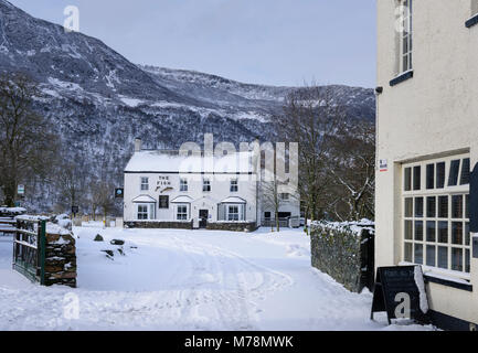 Winter verschneite Dorf Straße, die zu den Fischen Inn im Buttermere Im englischen Lake District Stockfoto