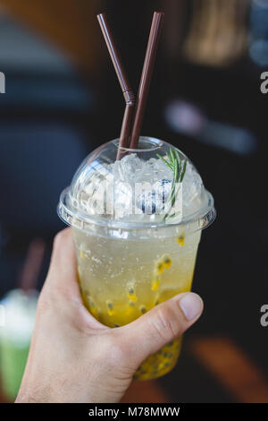 Hand mit Passionsfrucht mit Soda auf Kunststoff Glas mit zwei Stroh in Cafe Stockfoto