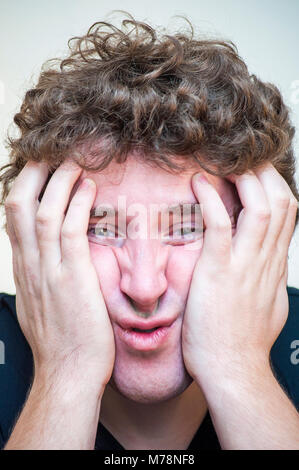Porträt der jungen schockiert konzentriert, der seinen gedrückt Gesicht mit beiden Händen auf weißem Hintergrund umfasst. Stockfoto