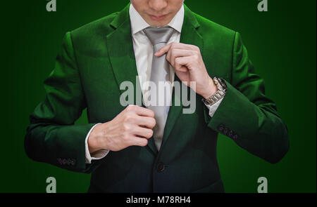 Unternehmer im grünen Anzug Krawatte binden, auf dunkelgrünem Hintergrund. Umwelt und Landwirtschaft Stockfoto