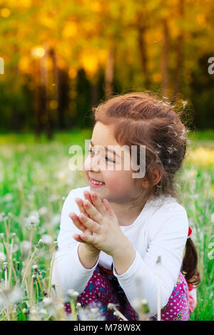 Schöne kleine Kind lächelnd mit Löwenzahn Blume im Sommer Park bei Sonnenuntergang Stockfoto