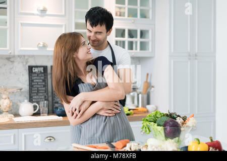 Reizende junge Paar Vorbereitung gesunde Mahlzeit in der modernen Küche. Mann umarmt Frau romantisch in Morgen in der Küche. Stockfoto