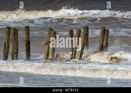 Wellen, die durch gebrochene Deckwerken, Walcott Norfolk Stockfoto