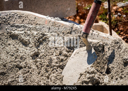 Baustelle mit Arbeiter mit Kelle nassen Zement von schubkarre auf Zement zu verbreiten Bausteine einer Betonwand mit Stahlstangen zu bauen Stockfoto