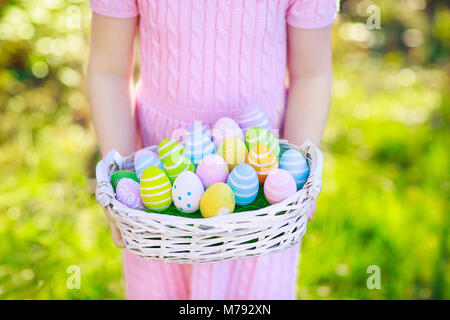 Ostereiersuche. Kleines Mädchen mit Eier legen. Kinder auf der Suche nach Süßigkeiten und Schokolade am Ostermorgen im Garten. Kind mit Feder Pastell decoratio Stockfoto