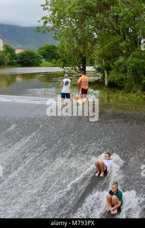 Kinder spielen im fließenden Wasser als Wasser Kaskaden über Aplins Wehr nach Stürmen und Starkregen, Aplins Wehr, Townsville, Queensland, Australien Stockfoto