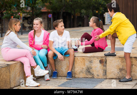 Zwei Jungen und drei Mädchen sind Kommunikation über Fußball auf Spaziergang im Park. Stockfoto