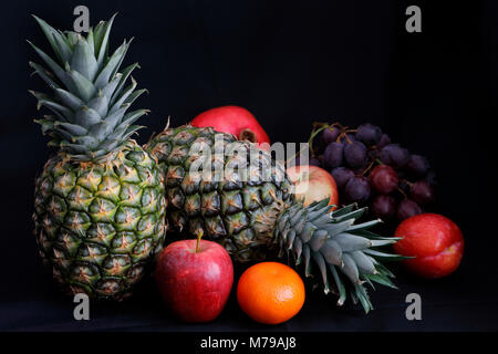 Dunkle Essen - Chiaroscuro Beleuchtung auf Ananas, Trauben, Pflaumen, Äpfel, Granatäpfel und Kalk mit dunklem Hintergrund und Kopie Raum Stockfoto