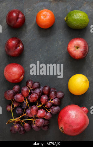 Dunkle Essen - Chiaroscuro Trauben, pomegranite, Zitrone, Apfel, Limette, Mandarine und Pflaume auf schiefer Hintergrund in eine Grenze mit Kopie Raum im Zentrum Stockfoto