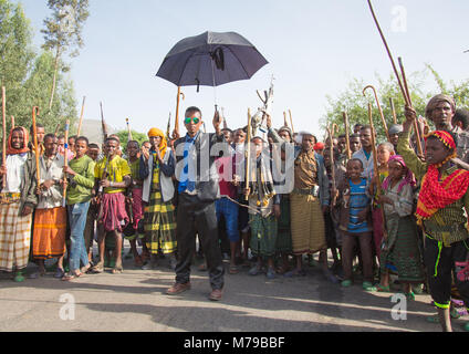 Eine oromo Bräutigam mit Sonnenbrille und ein Regenschirm, Tanzen und gerne feiert seine Hochzeit mit seiner Verwandten Männer und Jungen, Oromo region, Sambate, Stockfoto