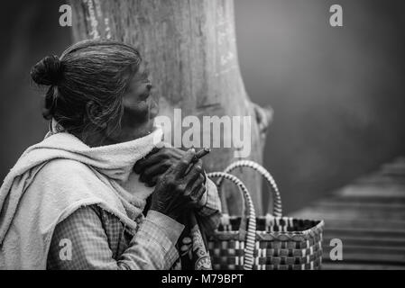 MANDALAY, MYANMAR - Dezember 11, 2017: Alte faltige Frau raucht eine cheroot Zigarre auf U Bein Holzbrücke in Mandalay, Myanmar. Schwarze und weiße Ton Stockfoto