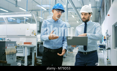 Leiter der Abteilung hält Laptop und Diskutieren Produkt Details mit Chief Engineer, während Sie durch moderne Fabrik gehen. Stockfoto