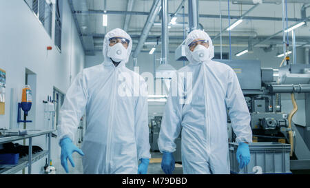Zwei Ingenieure/Wissenschaftler in Hazmat Sterile passt zu Fuß durch technologisch fortschrittlichen Fabrik/Labor. Saubere High-Tech-Umgebung mit CNC Stockfoto