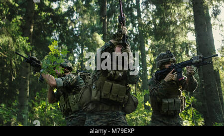 Drei voll ausgestatteten Soldaten tragen Camouflage Einheitliche angreifenden Feind, Sie in der Haltung, die Gewehre schießen. Militärische Operation. Stockfoto