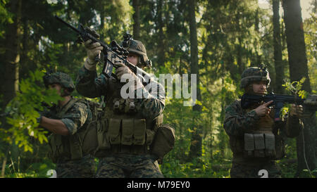 Drei voll ausgestatteten Soldaten tragen Camouflage Einheitliche angreifenden Feind, Sie in der Haltung, die Gewehre schießen. Militärische Operation. Stockfoto