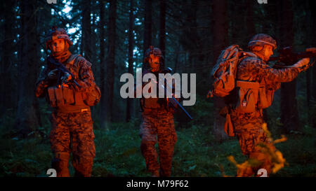 Gruppe von fünf voll ausgestatteten Soldaten in der Tarnung auf eine Aufklärung militärische Nacht Mission. Sie sind erleuchtet von roten Streulicht und durch dichten Wald bewegen Stockfoto