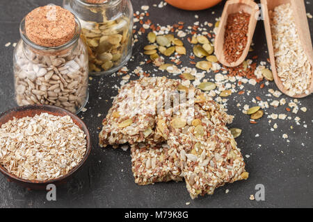 Gesunde Snack - knusprig Cornflakes Cookies auf schwarzen Steintisch und Zutaten: Haferflocken, Leinsamen, Kürbis-, Sonnenblumen-, Sesam. Diät crispy Cracker. S Stockfoto