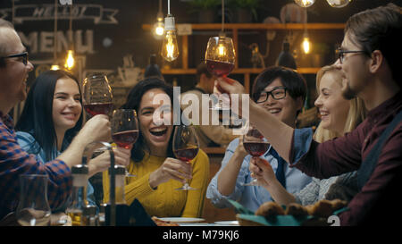 Vielfältige Gruppe von Freunde Feiern mit einem Toast und Clink angehoben Weingläser in der Feier. Schöne junge Leute haben Spaß in der stilvollen Bar Stockfoto