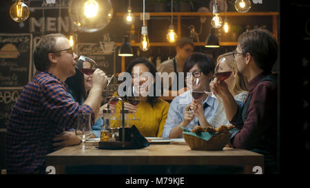 Vielfältige Gruppe von Freunde Feiern mit einem Toast und Heben Weingläser in der Feier. Schöne junge Leute haben Spaß in der stilvollen Bar/Restaurant. Stockfoto